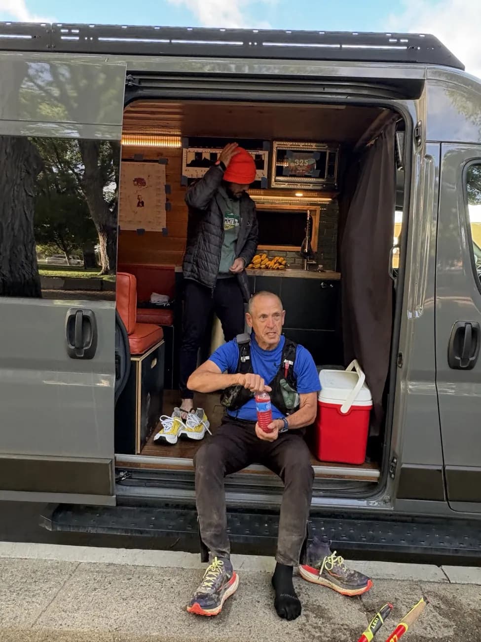 Paul James Johnson, in trail running gear and a hydration vest, sitting in the back of a crew van at an ultramarathon